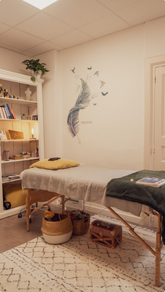 Salle de soin avec une table de massage, des objets et des livres.